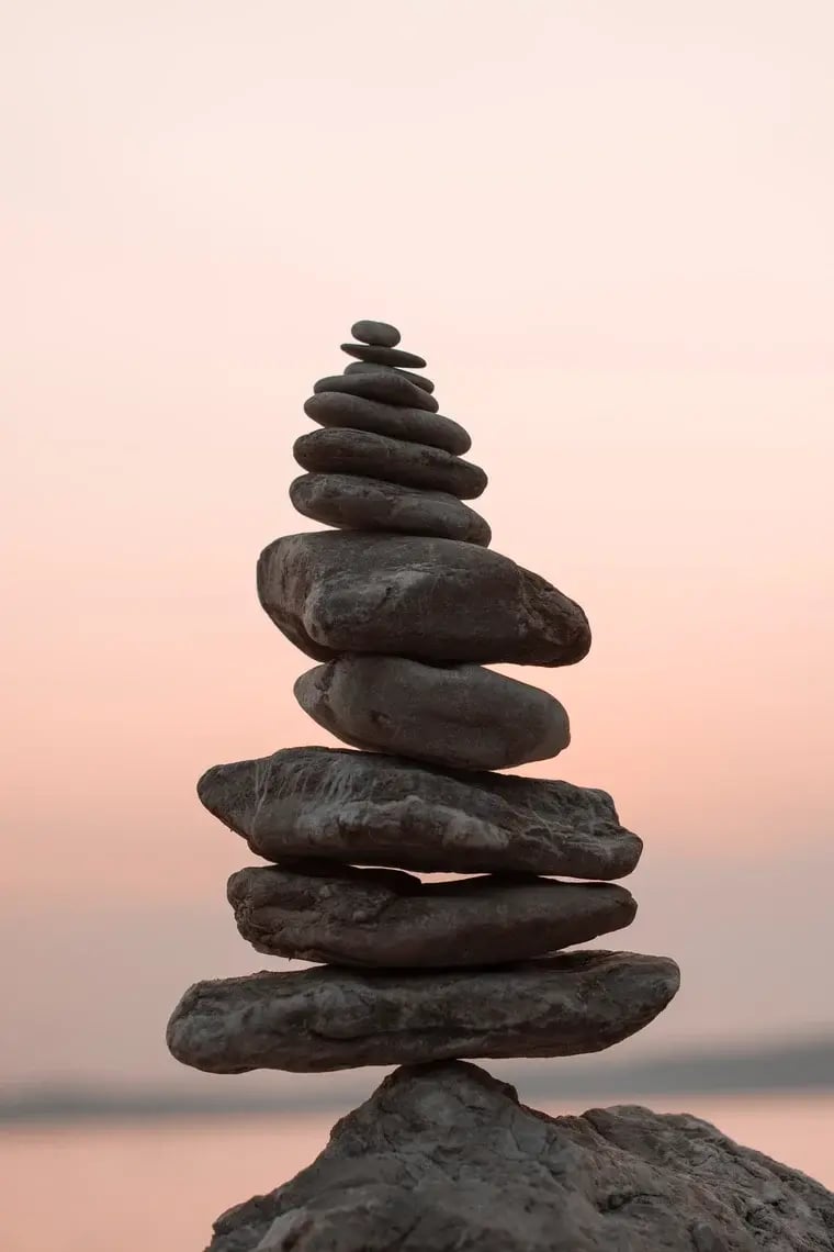 A pile or rocks are perfectly balanced on top of each other against a pink sky backdrop.