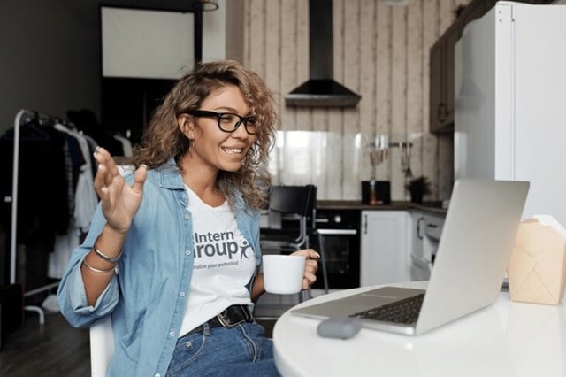 A woman in a The Intern Group t-shirt sits at a table with a laptop