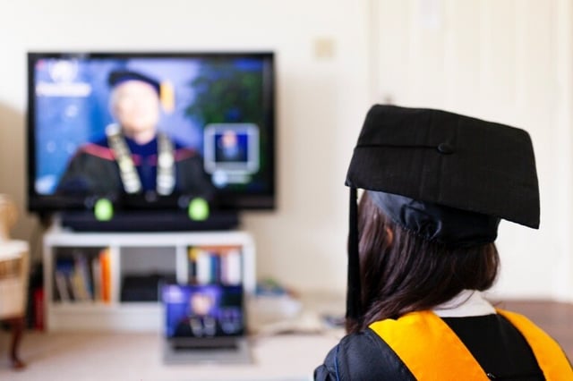A girl in graduation robes attends a remote commencement ceremony