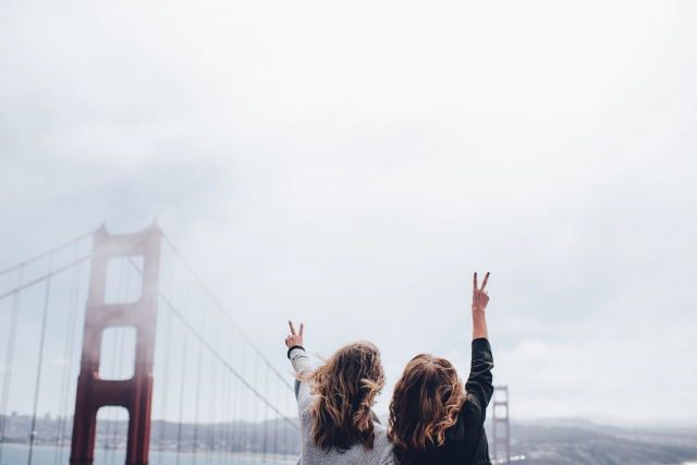 two women hold up peace signs in front of the Golden Gate Bridge