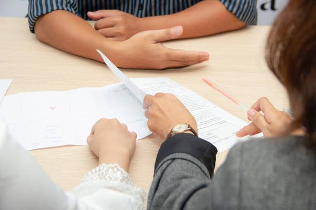 Three people discuss documents at a table.