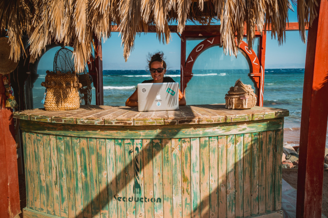 A woman works on a laptop in a beach hut.