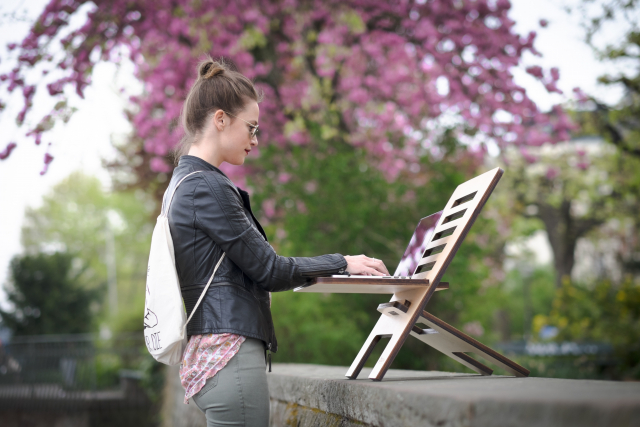A woman works on a laptop outside at a standing desk