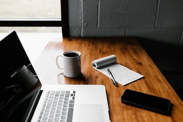 A laptop, cup of coffee, and a notebook on a desk as someone prepares their job application