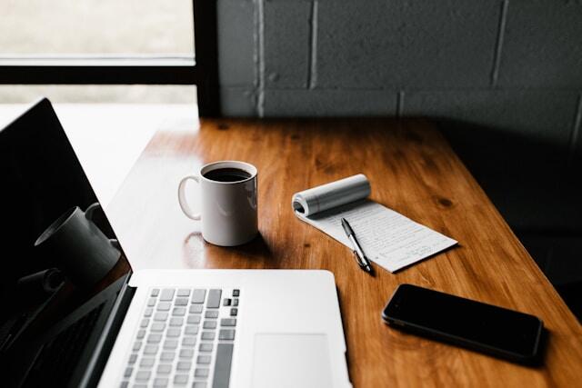 A laptop, cup of coffee, and a notebook on a desk as someone prepares their job application