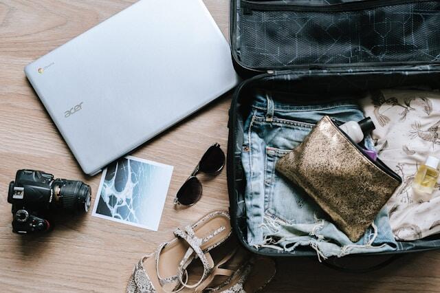 A suitcase being packed for a trip abroad with a laptop and a camera beside it.