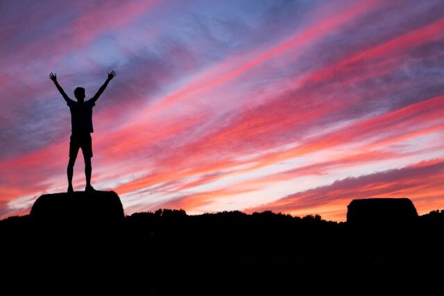 A young professional standing on top of a rocky landscape at sunset.