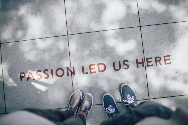 Two pairs of shoes standing on a sidewalk next to painted words that say "passion led us here."