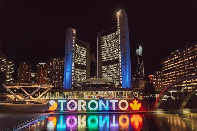 Toronto, Canada at night with 'Toronto' lit up in bright lights and reflecting in the water below.