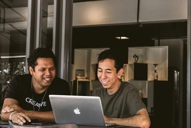 Two young professionals work and laugh together at a Macbook