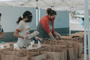 Young professionals making food parcels in the field during their non-profit internship.