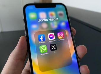 A mobile phone showing common social media apps like Facebook, Instagram, and X.