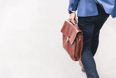 A young professional walking into a new job, holding a leather laptop bag.