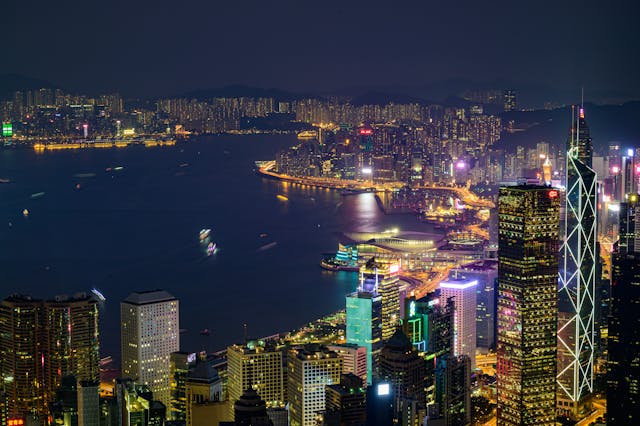 A view of Hong Kong's skyline at night, skyscrapers and buildings lit up against the dark.