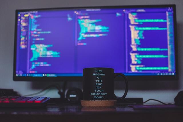 A mug in front of a computer. The mug says 'life begins at the end of your comfort zone'