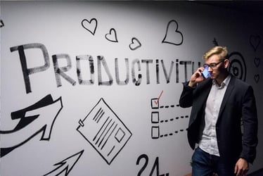 A man in a suits talks on the phone next to a wall which has the word 'Productivity' painted on it.