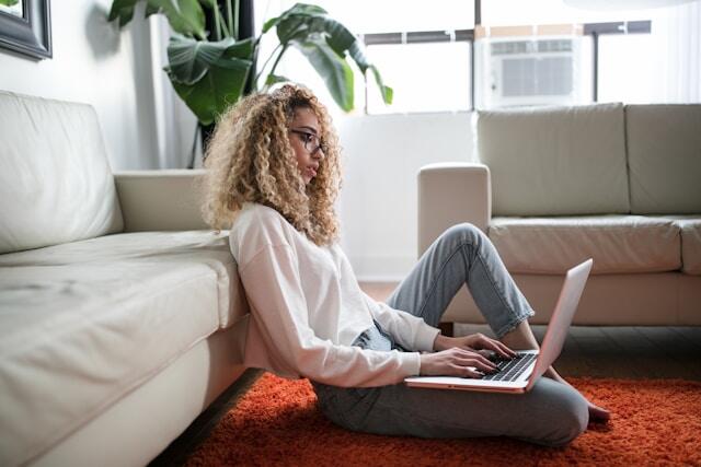 A young professional works on a laptop, sitting on the floor.