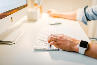 A close up of someone's hands as they type and use a mouse on a Mac computer.