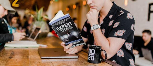 A young professional man reads a book on business improvement in a cafe.