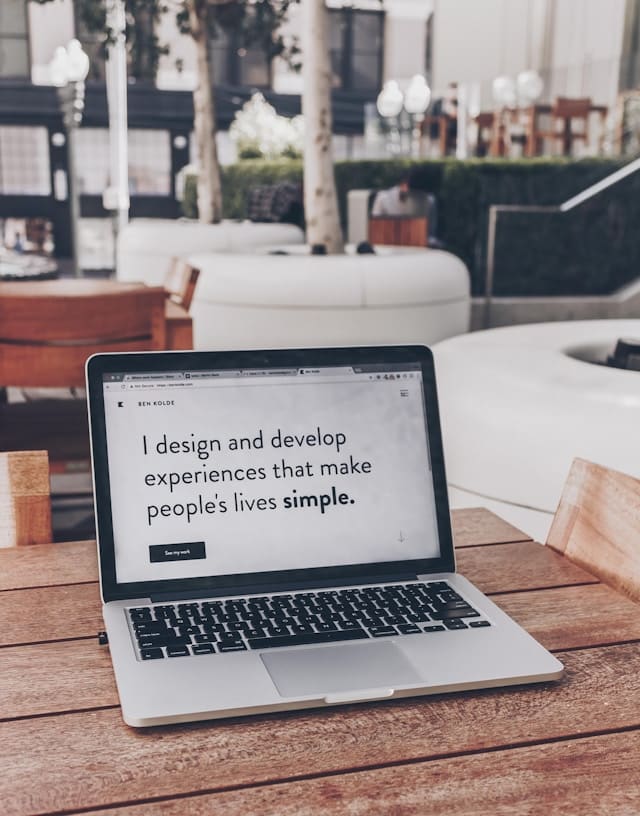 A laptop on a table. The screen shows someone's personal portfolio website and the quote from the website reads 'I design and develop experience that make people's lives simple.'