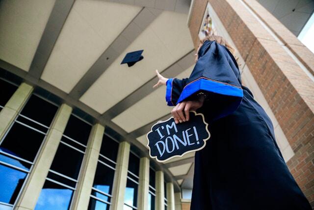 Somebody throwing their mortarboard into the air whilst holding a sign that reads 'I'm Done!'