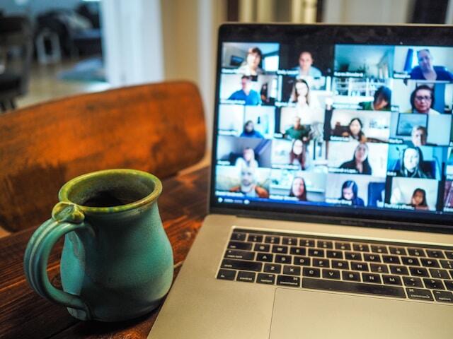 A laptop showing a Zoom call with twenty other people. The laptop is on a table next to a blue mug