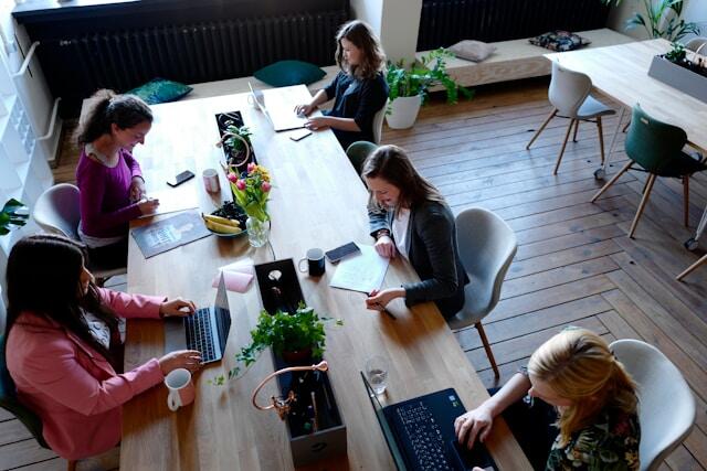 A group of young professionals in a shared office space as seen from above. They are working from laptops and notebooks.