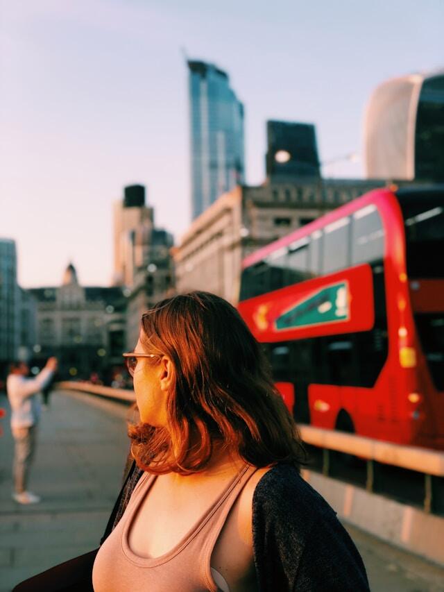 A woman looks over her shoulder. Behind her is a red London bus.