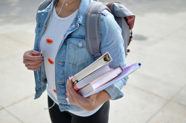 A student wears a heavy backpack and is carrying folders and textbooks in their arm as they go to university.