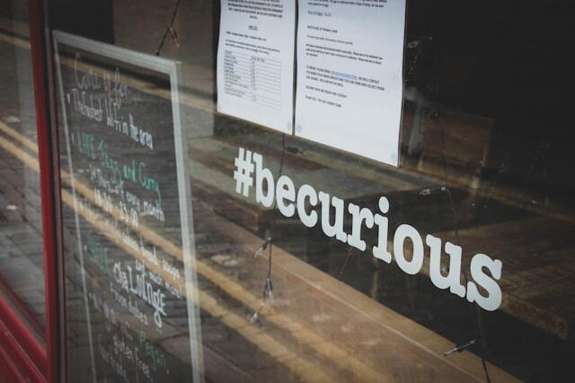 A sign in a window that reads "#becurious"