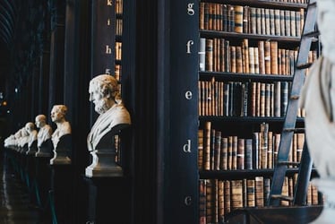 A darkly painted library with classical busts decorating each aisle.