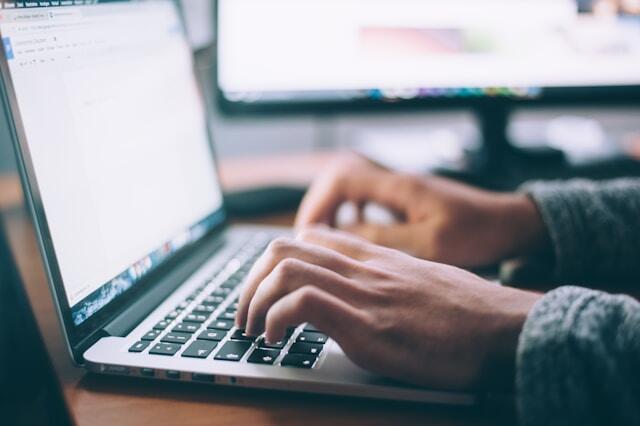 A close up of a man writing an email on a laptop Just his hands and keyboard are visible.