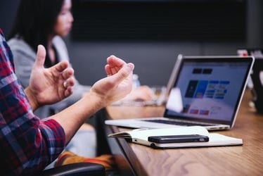 A close up of someone's hands during a business meeting or job interview. They are gesturing passionately in front of a laptop.