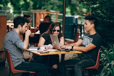 Three young professionals chat and work outside a coffee shop.