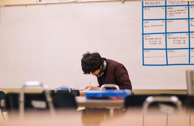 An older student sits in a classroom and writes in a notebook.