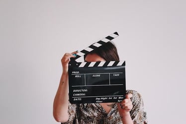 A person holds a film clapperboard in front of their face.
