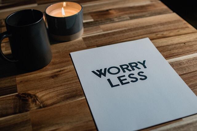 A piece of paper on a desk which reads 'worry less.' Beside it is a coffee cup and a lit candle.