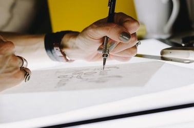 A close-up image of someone's hands as they draw with a mechanical pencil.