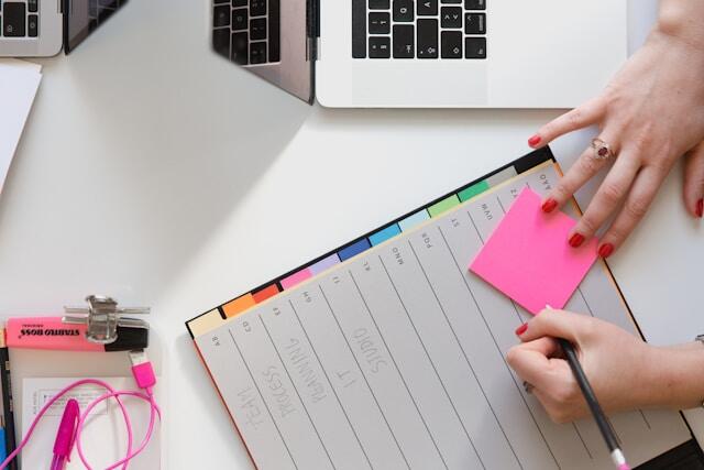 A young woman plans her work week using a desk planner and a set of post-it notes.