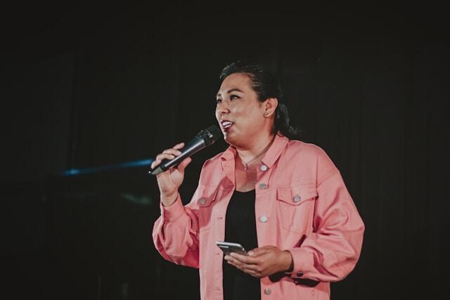 A woman performs a talk with a microphone and a phone in her hand.