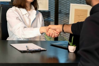 Two professionals shake hands over a desk at a business meeting.