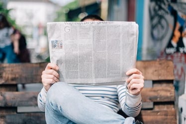 Somebody reading a newspaper on a bench.