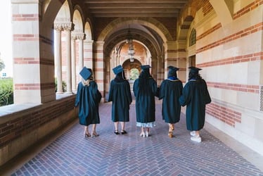 College students in graduation gowns walk down a hallway.