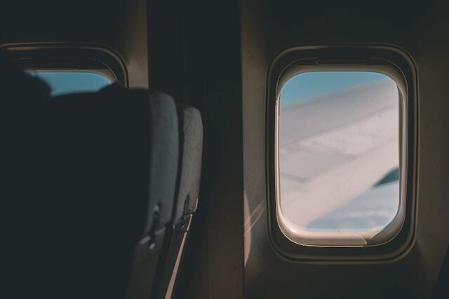 The inside of a plane, looking out of the window. The wing of the plane is visible through the glass.