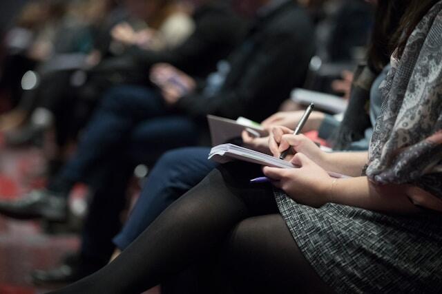 Professionals at a business networking event write down notes in notebooks.