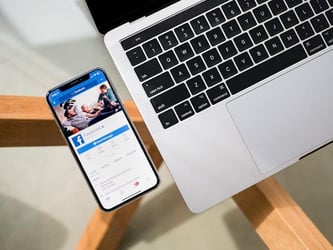 A laptop beside a phone which displays a Facebook profile.