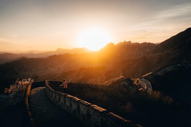 The sunset over the Great Wall of China. A man walks along the top of the wall.